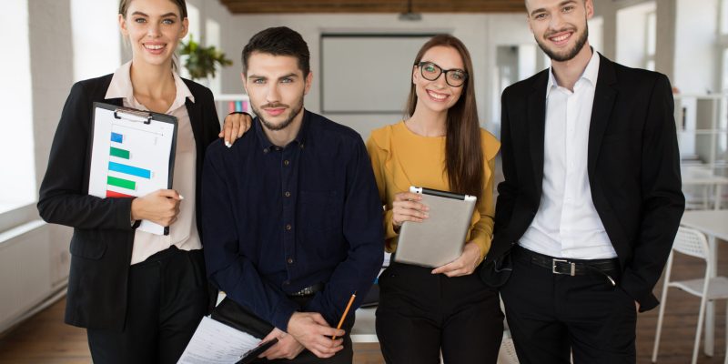 Group of young business people in classic suits happily looking in camera together spending time at work in modern office