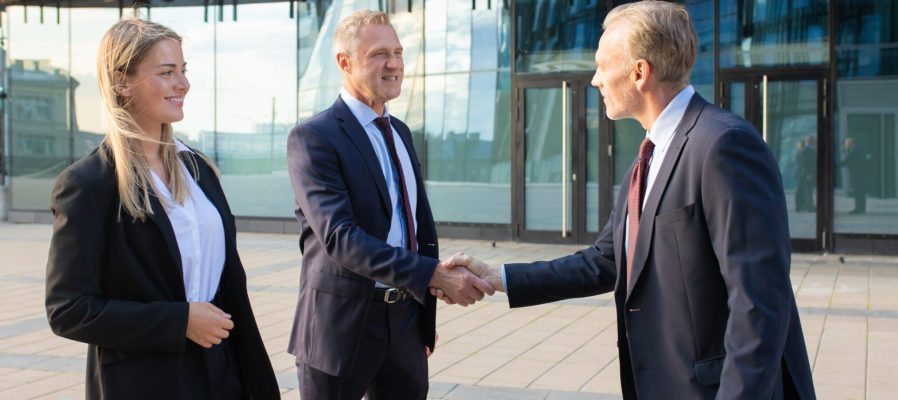 Positive business partners meeting at office building, shaking hands with each other. Side view, medium shot. Corporate communication or handshake concept
